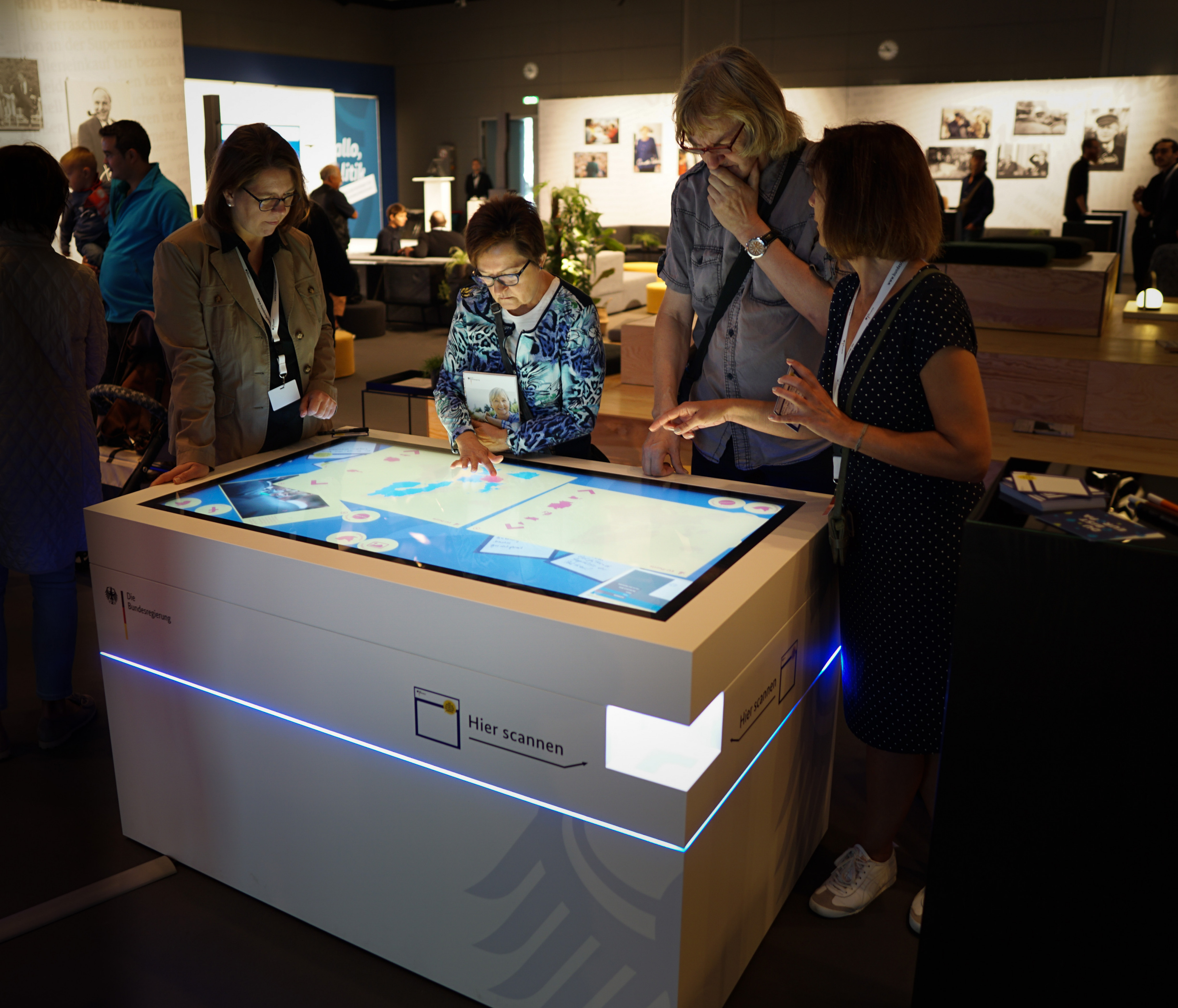 Eine Gruppe von vier Personen steht um einen Kubusförmigen Tisch, dessen Oberfläche ein Touchscreen ist. Auf dem Screen sind Informationen und Bilder zu sehen, welche sich die Gruppe ansieht.